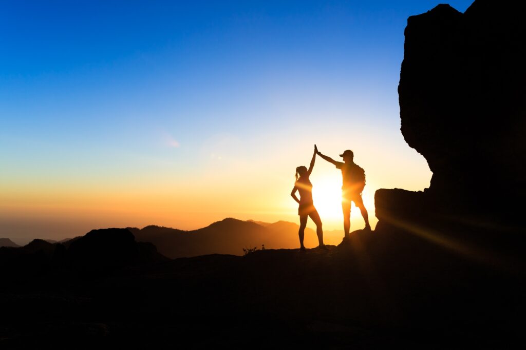 Zwei Personen geben sich ein High-Five beim Sonnenuntergang auf dem Berg – Symbol für Freundschaft, gemeinsame Erinnerungen und persönliche Verbindung in einer Trauzeugenrede