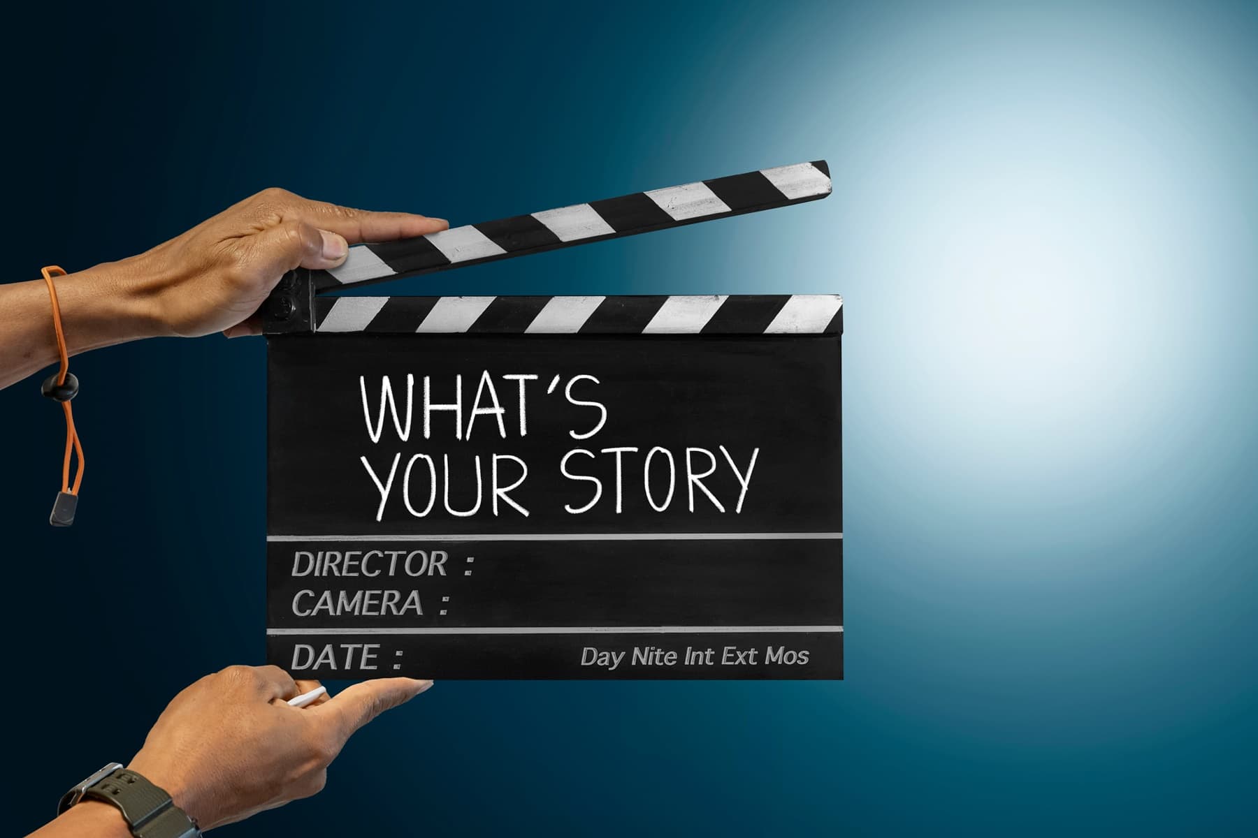 Zwei Hände halten eine schwarz-weiße Filmklappe mit der Aufschrift „What’s your story?“ vor blauem Hintergrund – Symbolbild für den Beginn einer persönlichen Geschichte im Storytelling oder in Präsentationen.